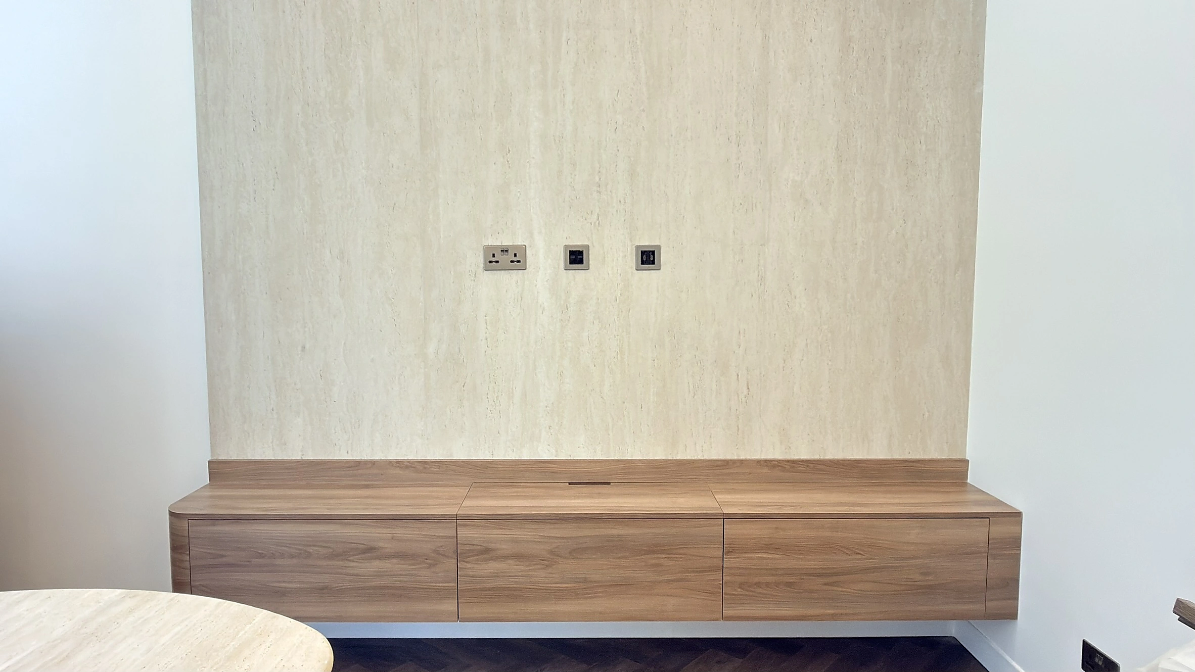 Floating walnut dining sideboard in Dubai set against a full-height travertine wall