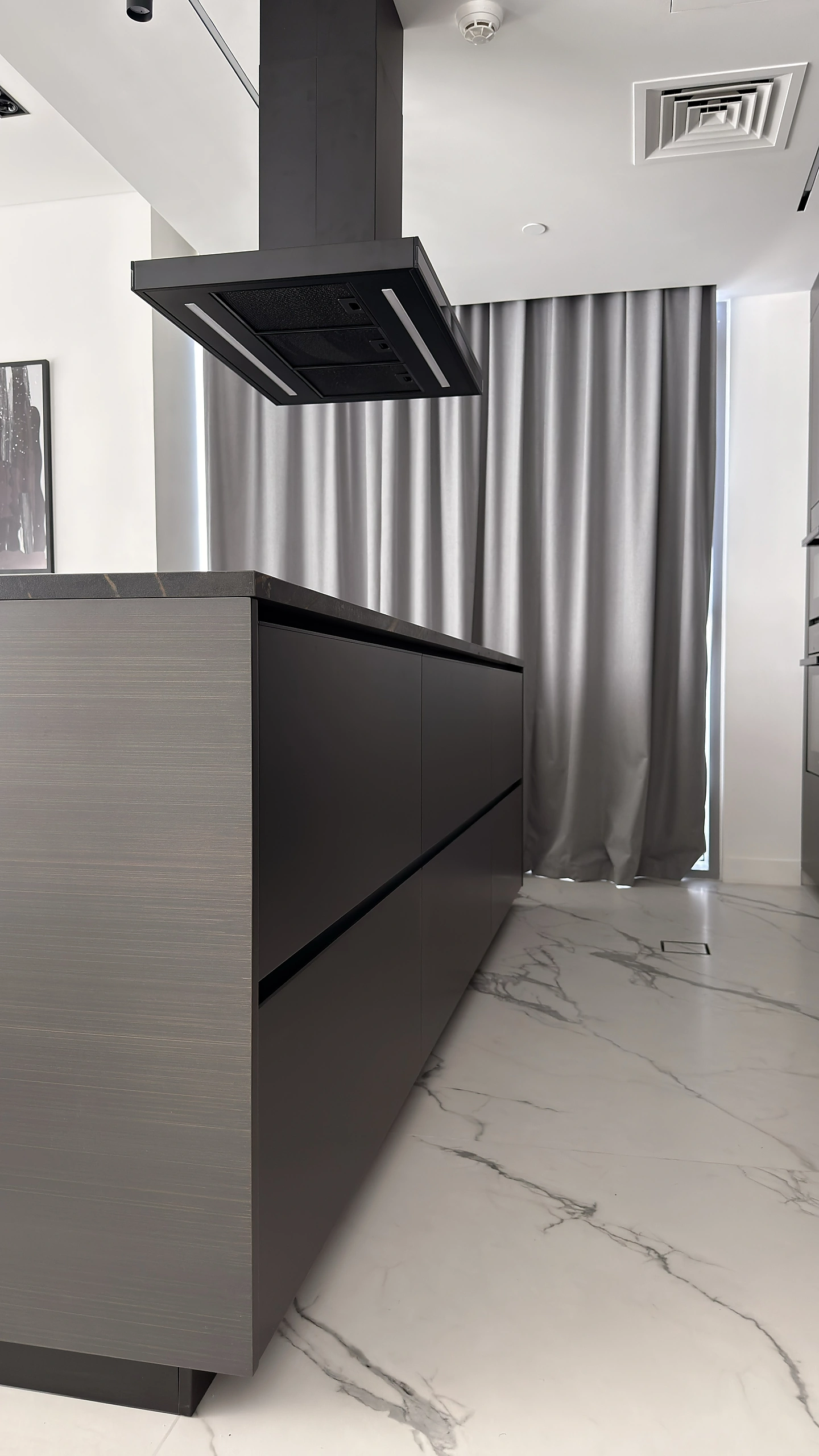 Handleless dark kitchen island in Dubai with a stone worktop and ceiling-mounted extractor