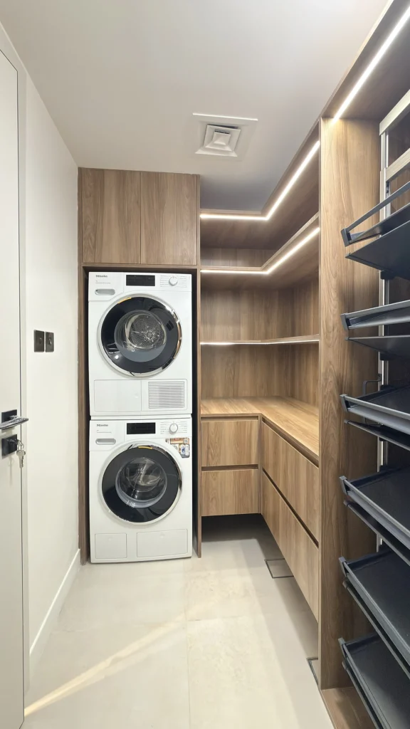 Laundry room fit-out in Dubai with walnut Egger cabinetry, stacked appliances and pull-out racks