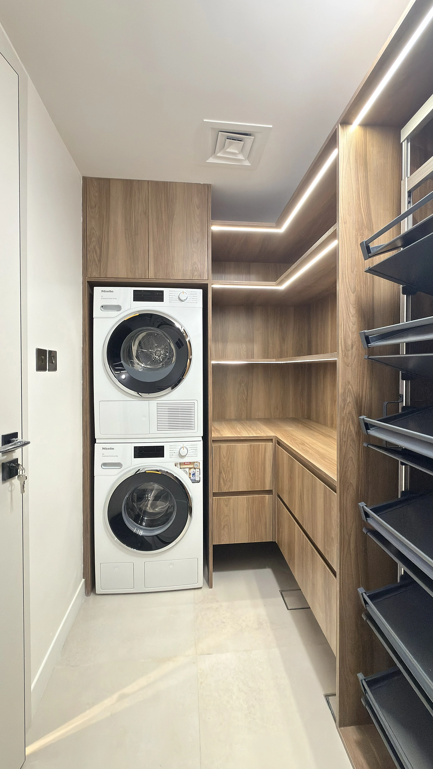 Laundry room fit-out in Dubai with walnut Egger cabinetry, stacked appliances and pull-out racks