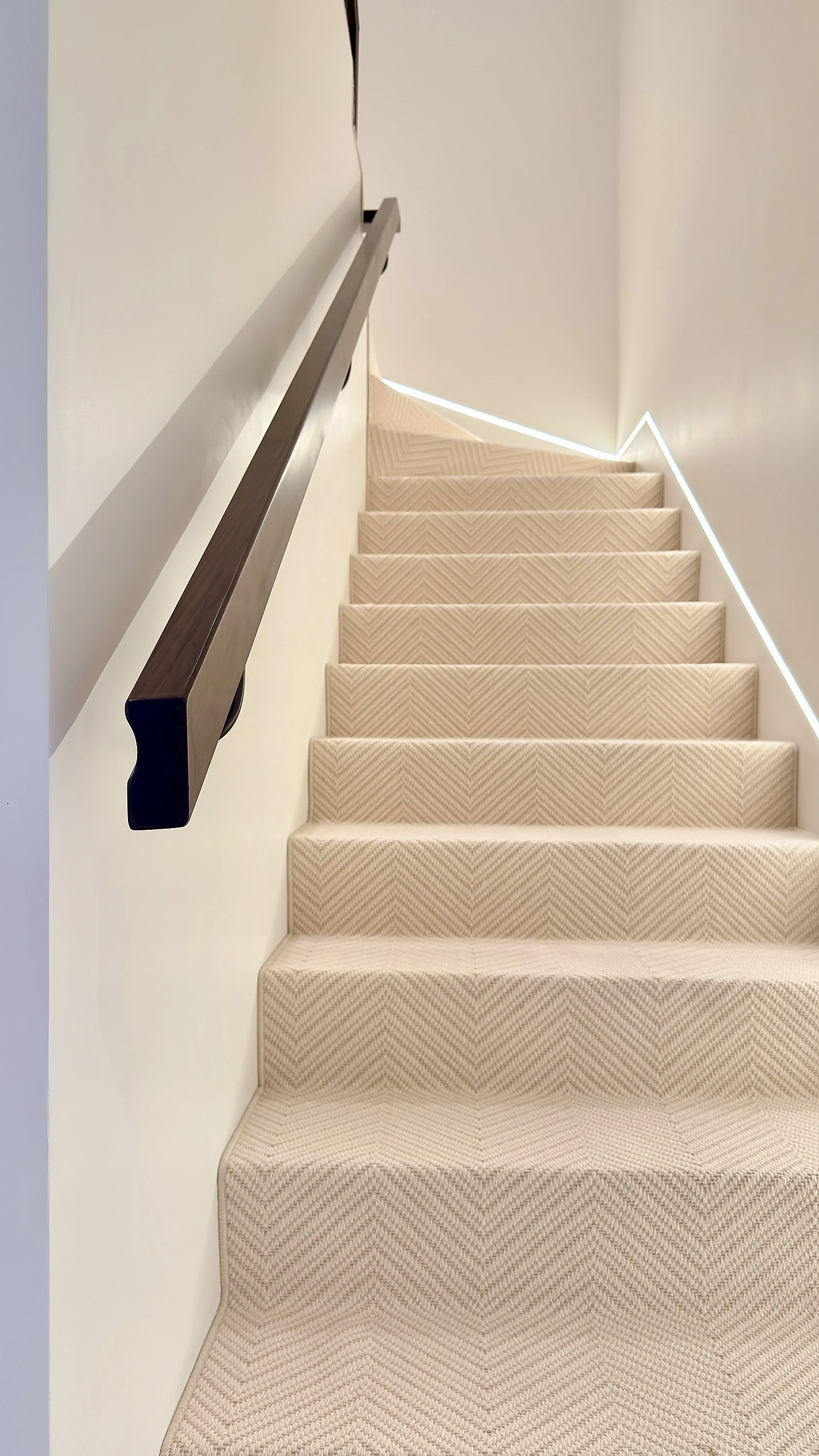 Staircase in Dubai with a solid white oak handrail, herringbone runner and recessed LED